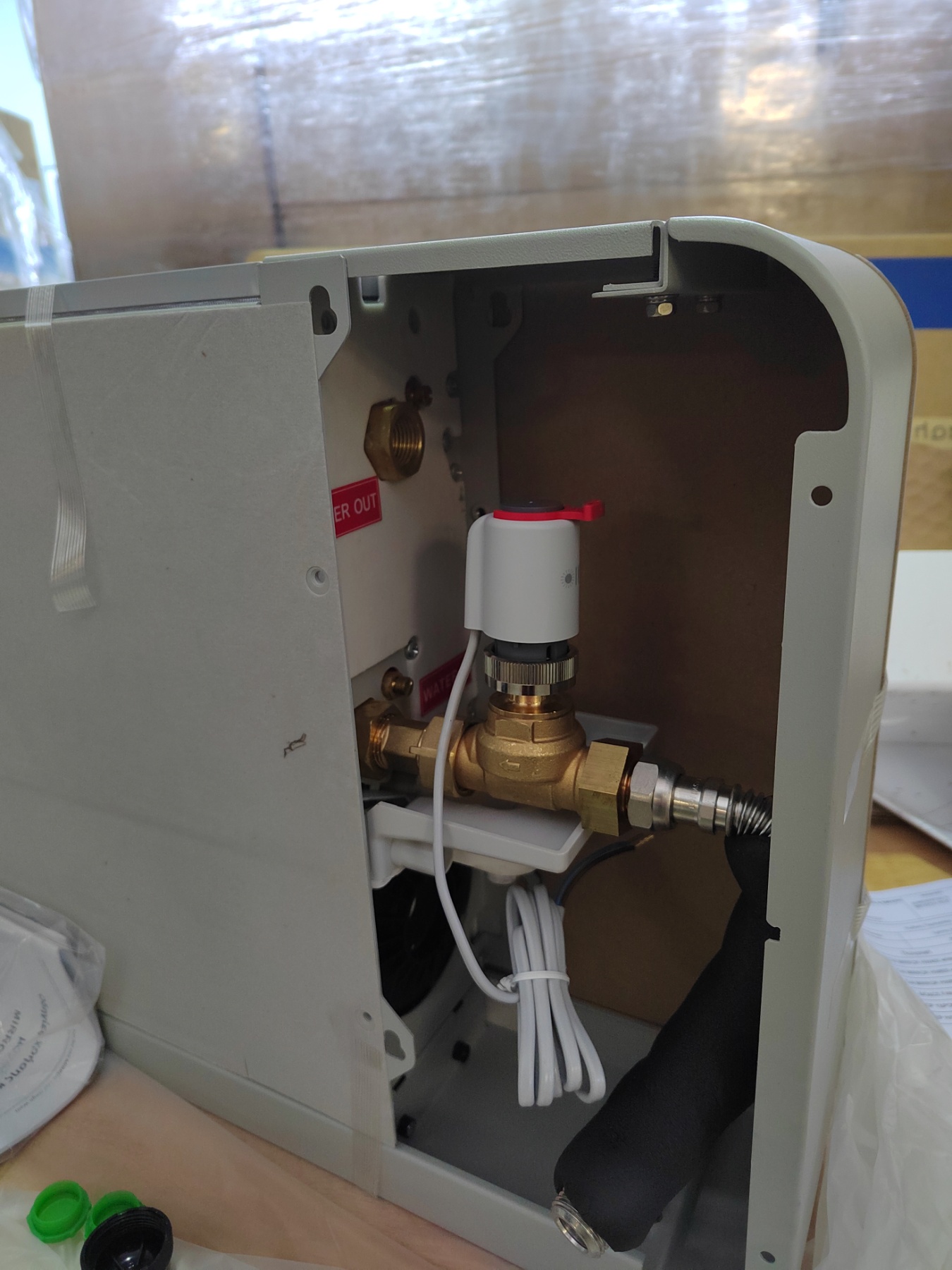 Interior view of a gray appliance with brass valve, white sensor, and copper plumbing connections inside a metal housing